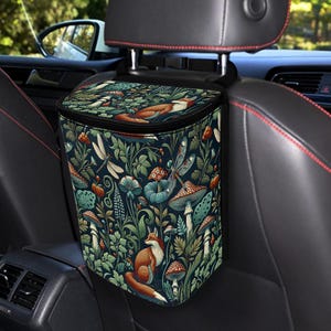 May include: A car trash bag with a whimsical forest design featuring foxes, mushrooms, and dragonflies in shades of green, blue, and orange. The bag is attached to the car's headrest and is designed to hold trash.