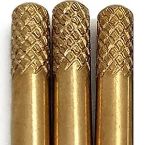 Könnte beinhalten: Drei goldfarbene Metall-Dübel mit einem Diamantmuster auf der Oberfläche. Die Dübel haben eine abgerundete Spitze und eine leicht verbreiterte Basis.