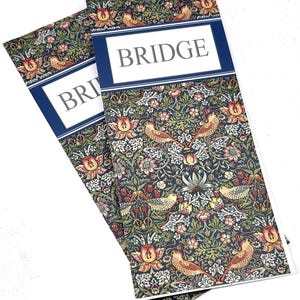 May include: Two rectangular bridge score pads featuring a dark blue background with a dense floral and bird pattern in shades of red, yellow, and green. Each pad has a white horizontal rectangular label with the word BRIDGE printed in black.