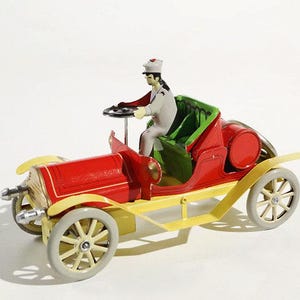 Può includere: Un'auto giocattolo vintage rossa, gialla e grigia, con una figura di guidatore. L'auto presenta una carrozzeria rossa, dettagli gialli e ruote grigie. Il guidatore indossa un'uniforme grigia e un cappello bianco.