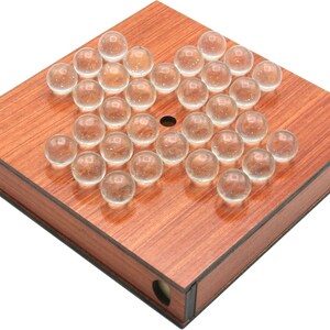 Puede incluir: Un tablero de juego de madera con un agujero en el centro y 37 canicas de vidrio transparentes dispuestas en un patrón. El tablero tiene un acabado de madera de grano marrón oscuro.