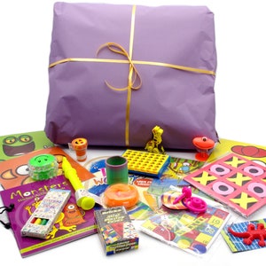 Può includere: Una borsa regalo viola piena di una varietà di giocattoli e giochi colorati per bambini. La borsa è legata con un nastro giallo. I giocattoli includono un libro, un gioco, un puzzle, uno spinner, una matita, un pastello, un adesivo, un animaletto di peluche e un insetto giocattolo.