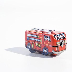 Könnte beinhalten: Ein rotes Spielzeugfeuerwehrauto mit einer Leiter auf dem Dach und zwei Feuerwehrleuten in der Kabine. Das Auto hat schwarze Räder und gelbe Scheinwerfer.