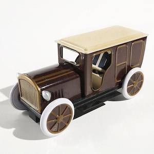 Può includere: Un'auto giocattolo vintage di colore marrone e oro con tetto bianco e ruote bianche. L'auto ha un interno dettagliato e un finestrino posteriore.