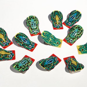 Könnte beinhalten: Eine Sammlung von 11 grün-gelben Frosch-Aufziehspielzeugen. Jeder Frosch ist mit schwarzen Punkten bemalt und hat rote Augen. Die Frösche sind in einem Kreis auf weißem Hintergrund angeordnet.