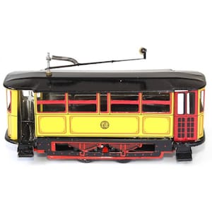 Può includere: Un tram giocattolo giallo e rosso con un tetto nero e un palo di trolley in metallo. Il tram ha una base e ruote nere e rosse.
