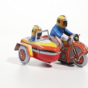 Op de afbeelding: Een rode en gele speelgoedmotorfiets met zijspan. De motorfiets heeft een blauwe en witte rijder met een gele helm. De zijspan heeft een gele en blauwe rijder met een gele helm.
