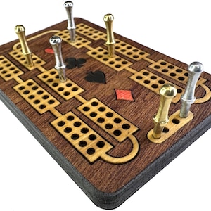 Op de afbeelding: Houten cribbagebord met een donkerbruine afwerking, met een reeks gaten en decoratieve kaartsymbolen. Het bord bevat gouden en zilveren metalen pinnen om te scoren. Een klassiek spel voor familieplezier.