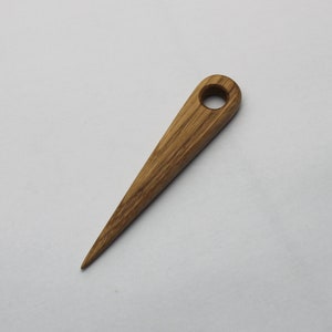 May include: A wooden awl, a tool with a pointed end and a hole in the handle. The awl is made of light brown wood and has visible wood grain.