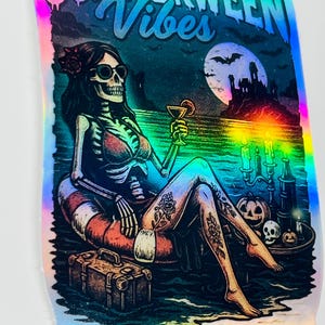 Puede incluir: Pegatina hologr&aacute;fica con un esqueleto descansando en un flotador, sosteniendo un c&oacute;ctel. La pegatina presenta el texto "Summerween Vibes" y "Spooky Year Round". El esqueleto tiene tatuajes y lleva gafas de sol.