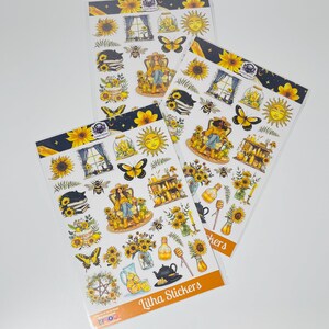 May include: Three sheets of stickers featuring a whimsical sunflower and bee theme. The stickers feature a woman sitting in a chair, a cat sleeping on a book, a beehive, a jar of honey, a teapot, lemons, and sunflowers. The text "Lilha Stickers" is printed on the bottom of the sheet.