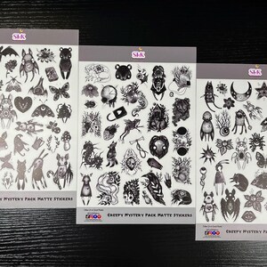 May include: Three sheets of black and white matte stickers with a creepy, gothic theme. Each sheet features a variety of illustrations, including creatures, plants, and symbols. The text on the sheets reads "Creepy Mystery Pack Matte Stickers".