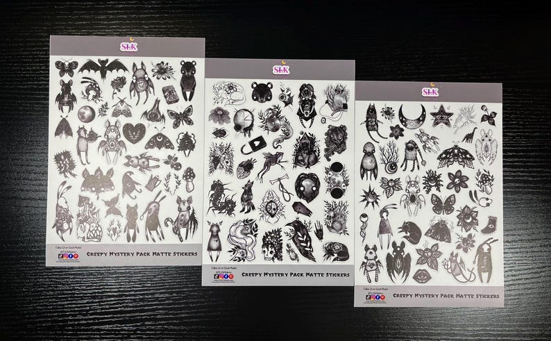 May include: Three sheets of black and white matte stickers with a creepy, gothic theme. Each sheet features a variety of illustrations, including creatures, plants, and symbols. The text on the sheets reads "Creepy Mystery Pack Matte Stickers".