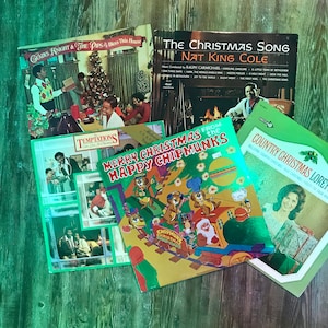 May include: A collection of vintage Christmas music albums featuring artists like Gladys Knight & The Pips, Nat King Cole, The Temptations, and The Chipmunks. The albums have green, red, and white covers with festive illustrations.