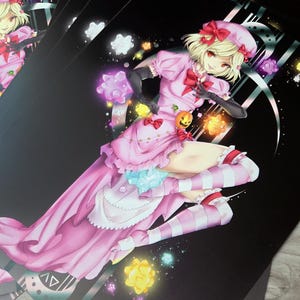 Puede incluir: Una impresión artística rectangular que muestra un personaje de estilo anime con cabello rubio, vestido rosa, boina a juego y medias a rayas. El personaje está rodeado de iconos brillantes y coloridos en forma de estrella sobre un fondo negro.