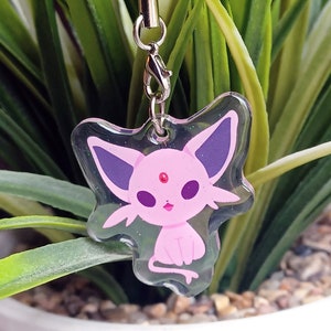 May include: A clear plastic charm with a pink and purple cartoon character. The character has a pink body, purple ears, and a pink gem on its forehead. The charm is attached to a black string.