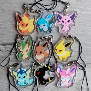 May include: A set of ten clear acrylic charms featuring different Pokemon characters. The charms are attached to black string lanyards. The characters include Eevee, Flareon, Jolteon, Vaporeon, Espeon, Umbreon, Leafeon, Glaceon, Sylveon, and a Pikachu.