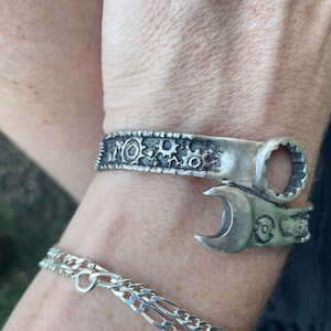 May include: A silver bracelet with a wrench design. The bracelet is decorated with gears and other mechanical details.