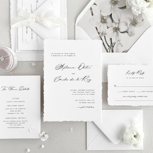 May include: Elegant wedding invitation suite with white paper and a floral envelope liner. The suite includes an invitation, RSVP card, details card, and envelope, with a ring box and flowers. The text is in black script.