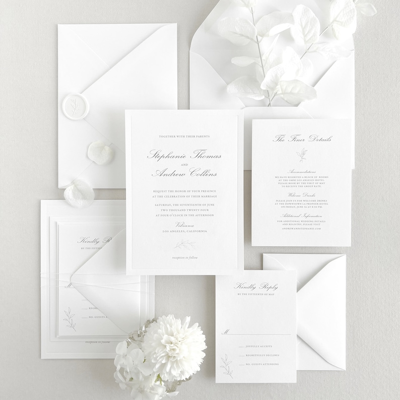 Invitation card features a thin de-bossed border, a classic script font for the names/venue, and a classic block font for the main text. A hand-drawn floral sprig is placed at the bottom of the card. Shown with matching insert cards + envelopes.