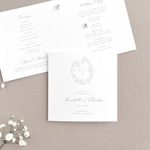May include: A white wedding invitation with a gray floral design and the text "Welcome to the wedding of Annabelle & Charles" with the date June 11, 2022 and the location Gallow Hall, Ashbourne, Derbyshire.
