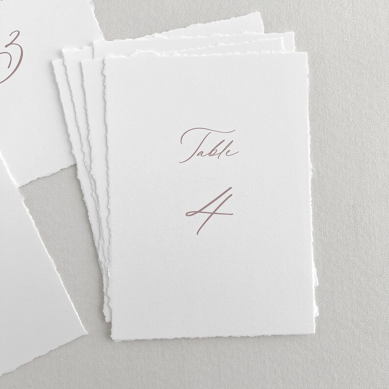 Pu&ograve; includere: Carta di numero di tavolo bianca con un carattere corsivo rosa che dice "Tavolo 4".