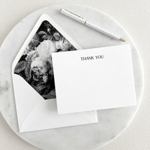 May include: A white envelope with a black and white floral design on the inside. The envelope is open and a white card with the text "THANK YOU" is inside.