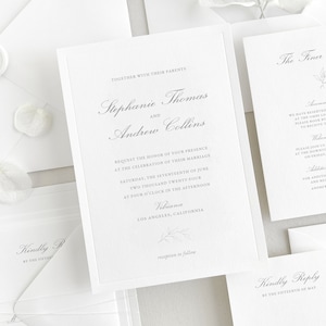 Invitation card features a thin de-bossed border, a classic script font for the names/venue, and a classic block font for the main text. A hand-drawn floral sprig is placed at the bottom of the card. Shown with matching white envelopes.