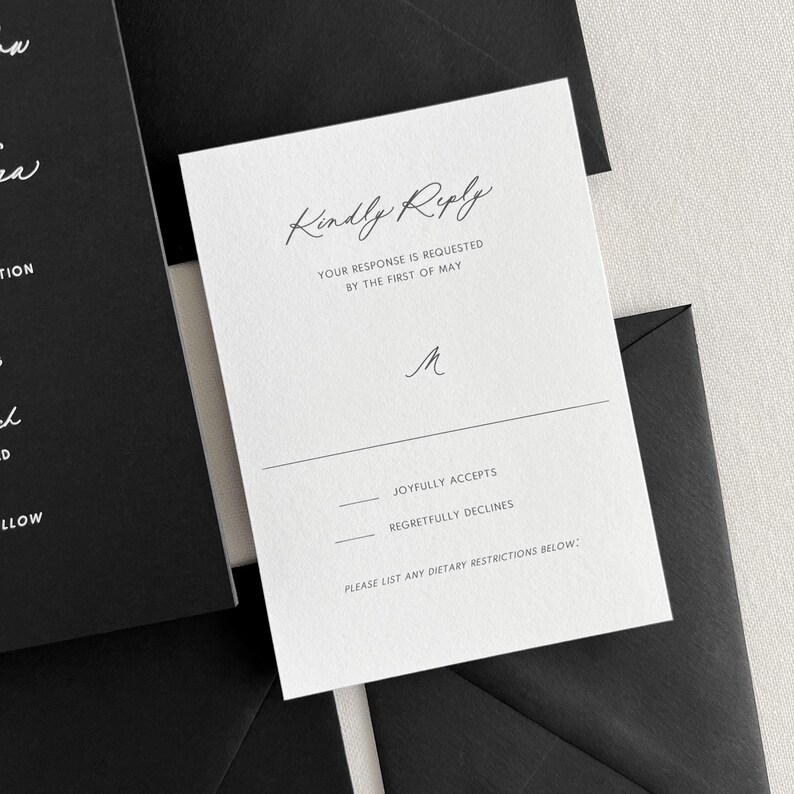 K&ouml;nnte beinhalten: Eine wei&szlig;e RSVP-Karte mit schwarzem Text. Die Karte lautet "Kindly Reply" und enth&auml;lt einen Abschnitt, in dem die G&auml;ste angeben k&ouml;nnen, ob sie "Joyfully Accept" oder "Regretfully Decline". Die Karte enth&auml;lt auch einen Platz f&uuml;r die G&auml;ste, um etwaige di&auml;tetische Einschr&auml;nkungen aufzulisten.