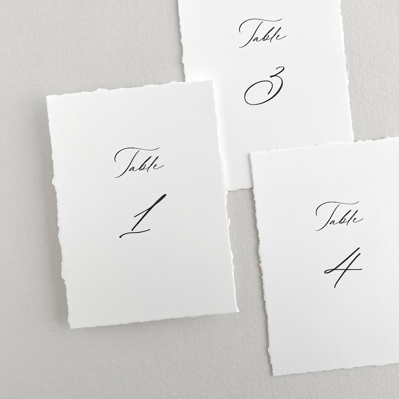 Pu&ograve; includere: Tre carte di numero di tavolo bianche con calligrafia nera. Le carte sono numerate 1, 3 e 4. Ogni carta ha la parola "Tavolo" scritta sopra il numero.