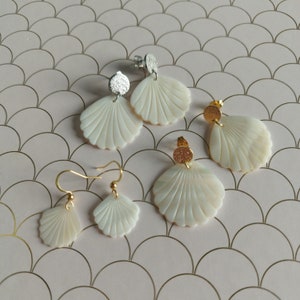 Peut inclure: Quatre paires de boucles d'oreilles en forme de coquillage avec des accents dorés et argentés. Les boucles d'oreilles sont sur un fond rose avec un motif de cercles qui se chevauchent.