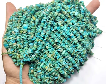 May include: A collection of turquoise chip beads in shades of blue and green. The beads are of irregular shape and size, strung together with a blue thread. The background is white.