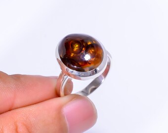 May include: A silver ring featuring a large, oval-shaped gemstone with a swirling pattern of brown, orange, and gold hues. The gemstone is set in a polished silver band.