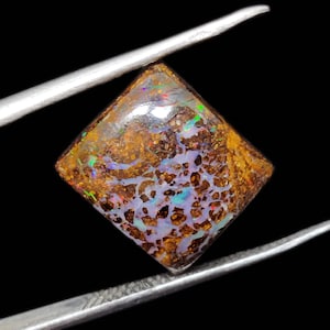 May include: A square-shaped opal gemstone with a brown, white, and iridescent colour pattern. The opal is set in a clear, faceted setting.