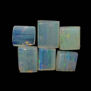 Puede incluir: Seis pequeñas piedras preciosas de ópalo rectangulares e iridiscentes. Los ópalos son de un blanco lechoso pálido con destellos de azul, verde y rojo.