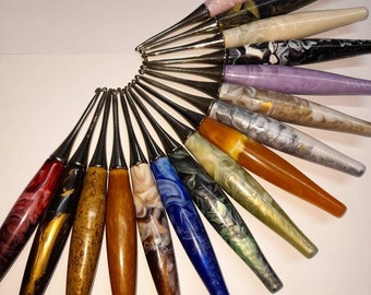 Peut inclure: Un ensemble de 18 crochets à crochet colorés avec des embouts en métal argenté. Les crochets sont disposés en éventail, les pointes pointant vers le centre. Les crochets sont faits de différents matériaux, dont le bois, le plastique et le métal. Les crochets sont tous de couleurs différentes, notamment le rouge, l'orange, le jaune, le vert, le bleu, le violet et le rose.