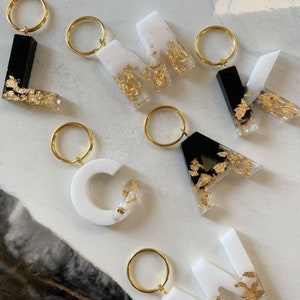 May include: A set of seven resin letter keychains with gold flakes. The letters are L, O, V, E, A, C, and K. Each letter is half black and half white. The keychains are attached to gold key rings.