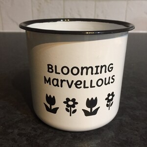 Puede incluir: Taza de esmalte blanco con borde negro y texto negro que dice "Blooming Marvellous" con cuatro ilustraciones de flores negras.