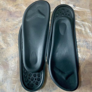 May include: Two black orthopedic shoe inserts with a textured surface. The inserts have a raised arch support and a contoured heel.