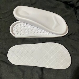 May include: A pair of white shoe insoles. One insole has a textured surface with small bumps. The other insole has a diamond pattern.