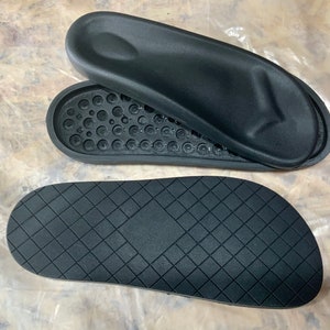 May include: Two black rubber soles for sandals. One sole has a textured surface with small circles. The other sole has a diamond pattern.