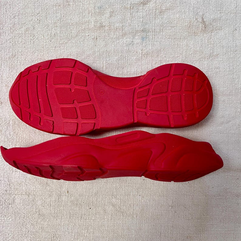 May include: A pair of red rubber shoe soles. The soles are textured and have a ridged pattern.
