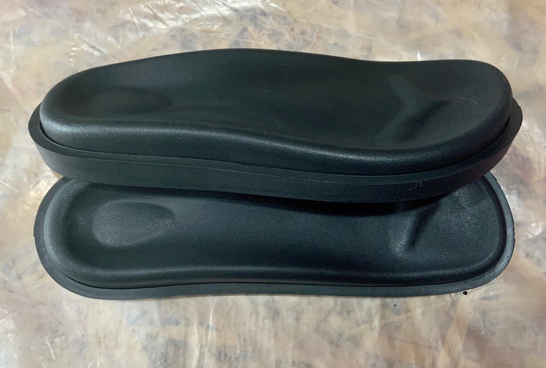 May include: Two black foam armrests for a chair or sofa. The armrests are oval shaped and have a smooth, slightly textured surface.