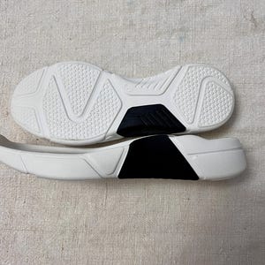 May include: A pair of white athletic shoes with black accents. The shoes are made of a textured material and have a rubber sole.