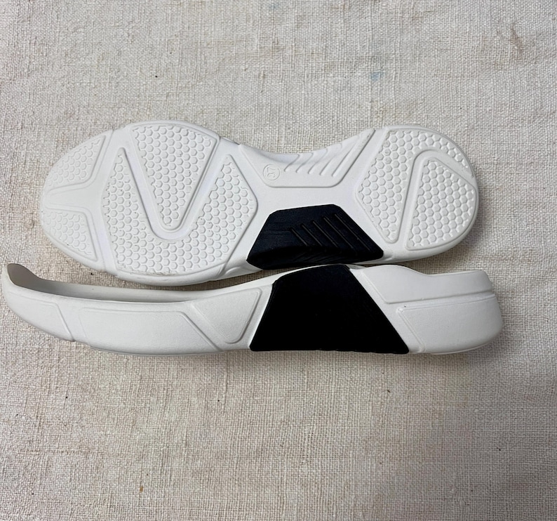 May include: A pair of white athletic shoes with black accents. The shoes are made of a textured material and have a rubber sole.