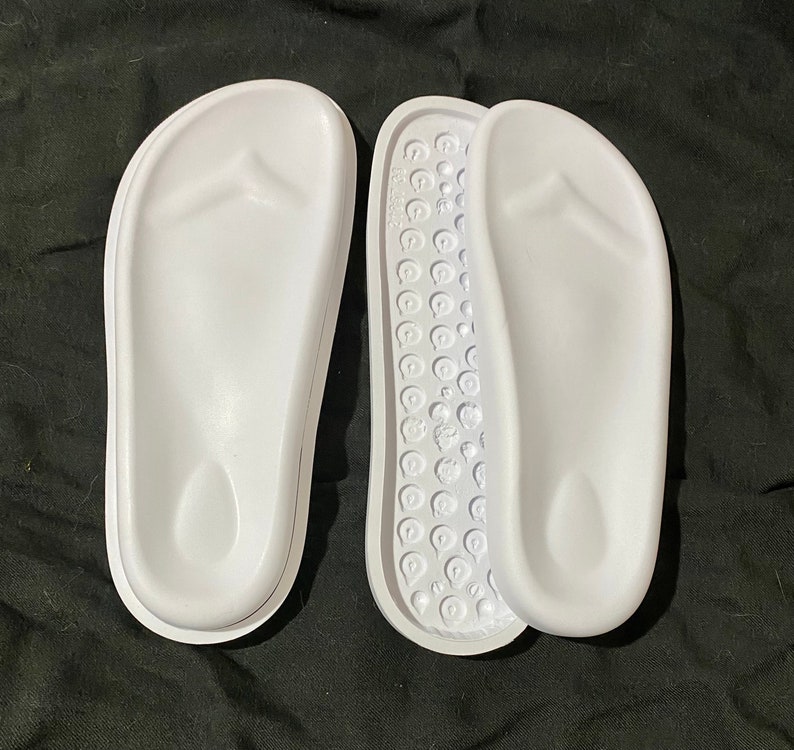 May include: A pair of white flip-flop sandals with a textured footbed. The sandals are made of a soft, flexible material and have a simple, classic design.