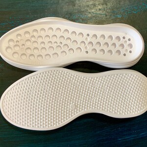 May include: Two white shoe soles, one with a circular pattern and the other with a diamond pattern.