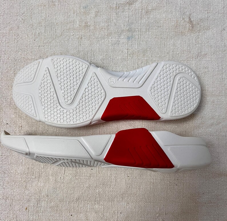 May include: A pair of white shoe soles with red accents. The soles are made of a textured rubber material and have a raised pattern on the bottom.