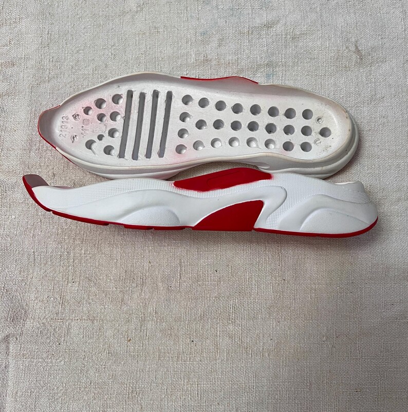 May include: White and red shoe sole with a textured bottom and a row of small holes. The sole is designed for a shoe with a thick, chunky platform.
