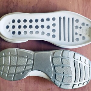 May include: A pair of white shoe soles, one with a textured rubber tread and the other with a smooth surface and a pattern of small holes. The sole with the holes has the text "38 1/3" printed on it.